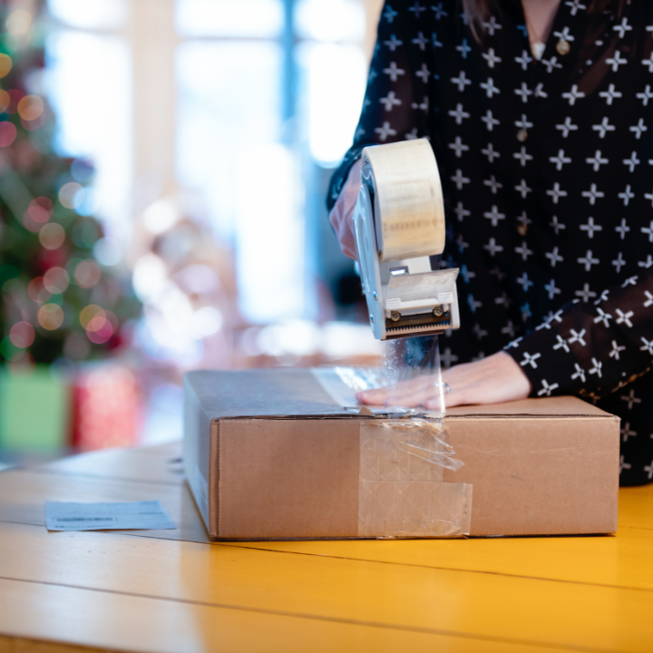 Person taping up box with holiday tree in background