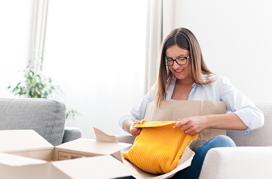 Engage return authorization. Female opening ecommerce delivery with yellow sweater.